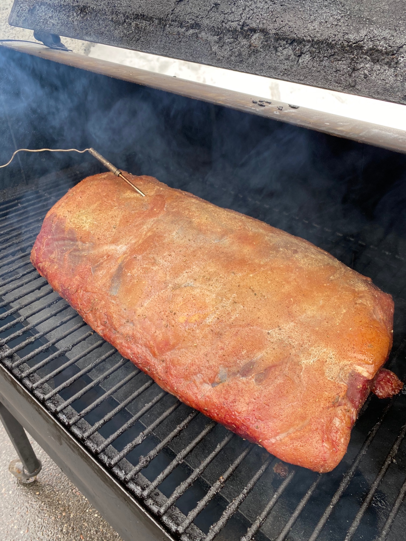 Seasoned pork loin smoking on a wood-fired grill